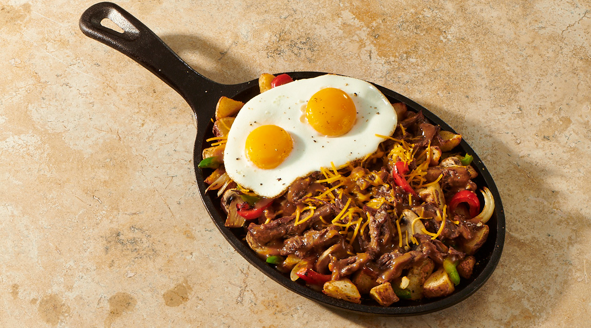 Braised beef breakfast skillet loaded with meat and roasted vegetable topped with two perfect sunny-side-up eggs.