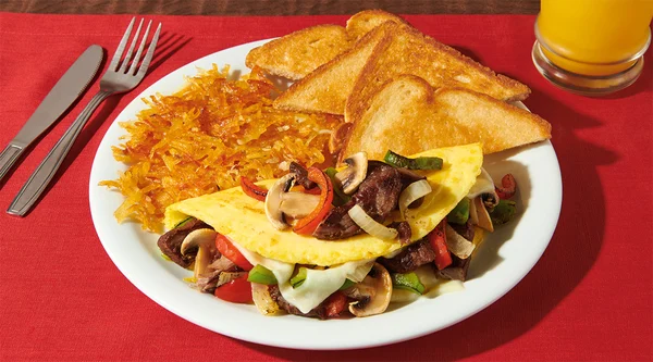 A folded omelet stuffed with mushrooms, onions, and bell peppers on a plate with toast and crispy hash browns.